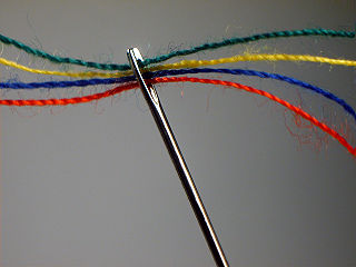 Una aguja enhebrada con cuatro hilos de diferente color.