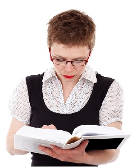 Mujer con gafas y pelo corto, sostiene un grueso libro en sus manos mientras lee.